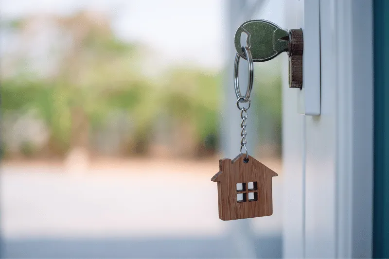 DSCR Home Loan 1 A silver key with a wooden house-shaped keychain is inserted into a door lock, with an outdoor background softly blurred.